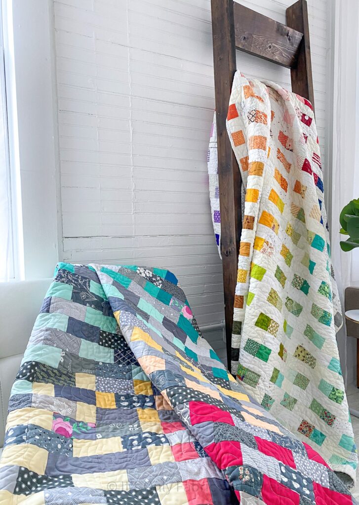 Rainbow quilts are displayed draping over a chair and on a wooden blanket ladder.