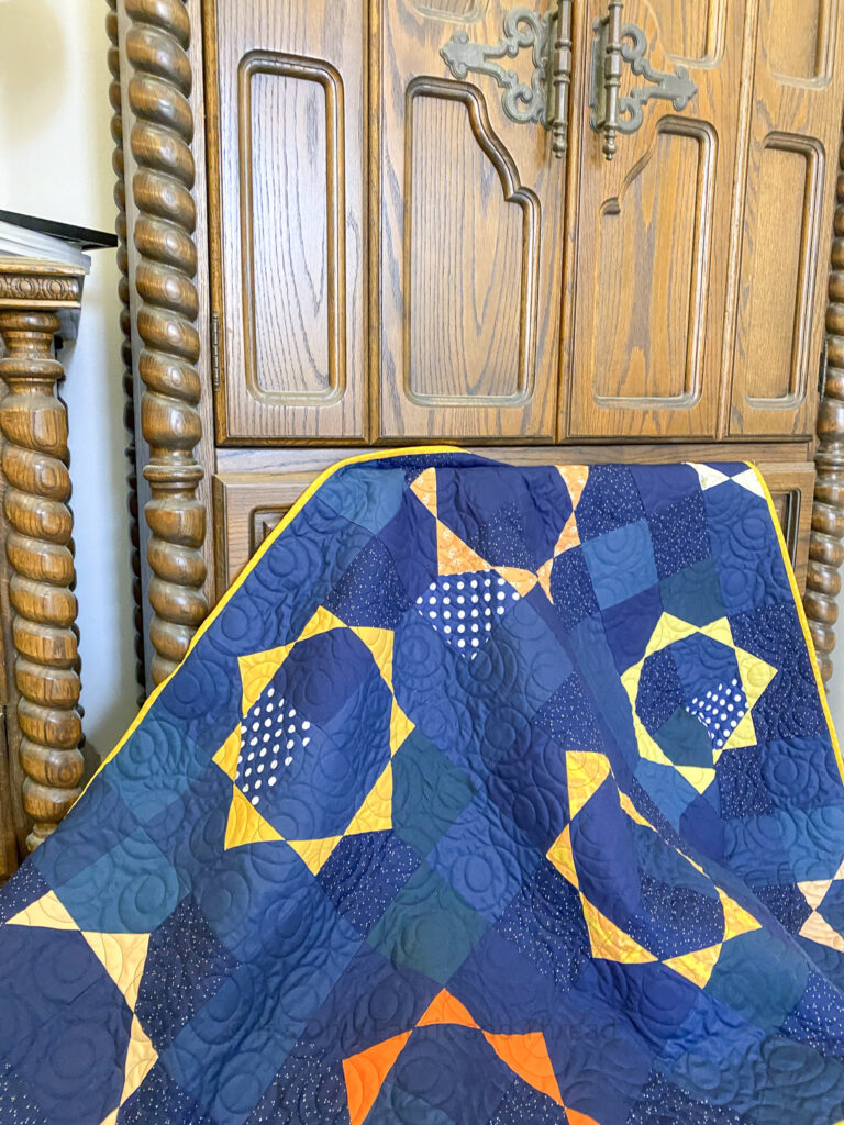 Blue and Yellow Quilt is draped in a wooden chest.