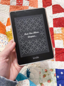 Amazon Kindle Paperwhite in front of a colorful quilt. The Kindle is showing a custom black and white lock screen.