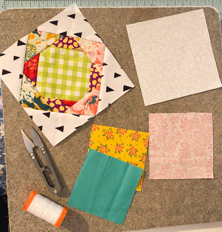 Scrap explosion quilt block lays flat on wool pressing mat with several squares of fabric laid out next to it.