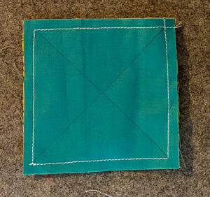 Turquoise quilt block with X drawn from corner to corner with a sewn white seam at 1/4".