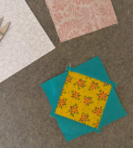 A turquoise and yellow economy quilt block on a wool pressing mat.