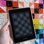 Amazon Kindle Paperwhite in front of a colorful quilt. The Kindle is showing a custom black and white lock screen.